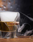 Glass with a bullet and liquid, surrounded by smoke on a wooden surface.